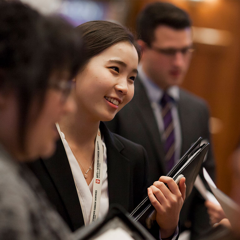 A student at a career fair event smiles while holding a leather portfolio folder.