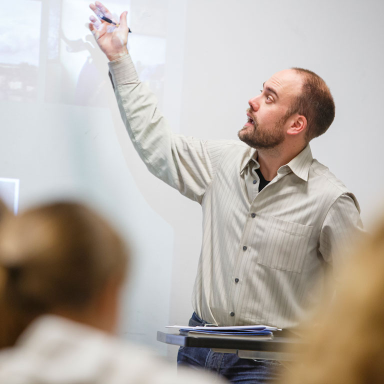 A faculty member gestures to a projected image during a class.